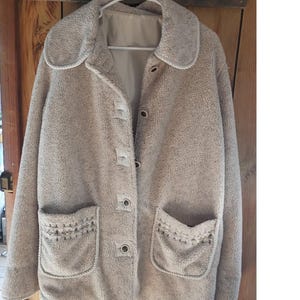 May include: A beige sherpa fleece jacket featuring a wide collar, a button-front closure, and two front patch pockets. Each pocket is decorated with a small, embroidered geometric pattern in dark thread along the top edge.