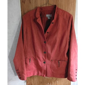 May include: A rust-colored jacket with a mandarin collar, button closure, and two front pockets with zippers. The jacket has long sleeves with button details at the cuffs. The brand name "Yessica Lane" is visible on the label.