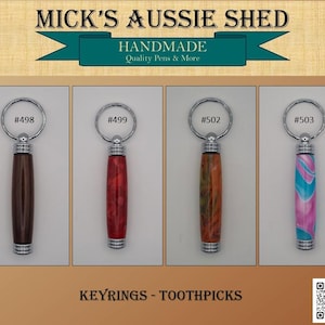 May include: Four cylindrical keyrings with metal hardware and split rings, labelled #498, #499, #502, and #503. The bodies feature distinct finishes: dark brown wood, marbled red, swirled orange and green, and a pink and blue wave pattern.
