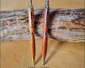 May include: Two handcrafted wooden pens labeled #283 and #284. The pen on the left features light brown wood with gold-tone metal hardware. The pen on the right features reddish-brown wood with silver-tone metal hardware and a clip.