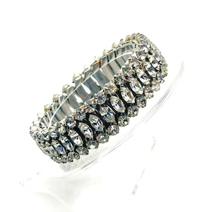 May include: A silver stretch bracelet featuring multiple rows of clear, sparkling rhinestones. The rhinestones are arranged in a repeating pattern, creating a dazzling display of light and reflection. This elegant piece is perfect for adding a touch of glamour.