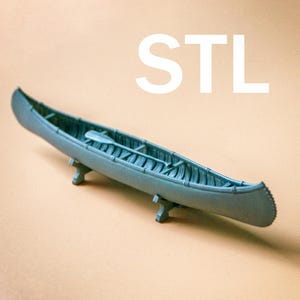 Może przedstawiać: Szary model kajaka wydrukowany w 3D z wiosłem w środku. Kajak stoi na dwóch małych podstawkach. Słowo "STL" jest wydrukowane białymi literami na beżowym tle.