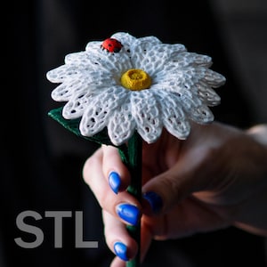 May include: A 3D printed white daisy flower with a yellow center and a red ladybug on one of the petals. The flower is held in a hand with blue nail polish.