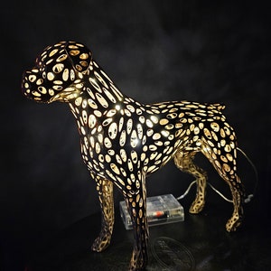 May include: A black metal dog sculpture with a light inside, creating a patterned effect. The sculpture is standing on a black surface.