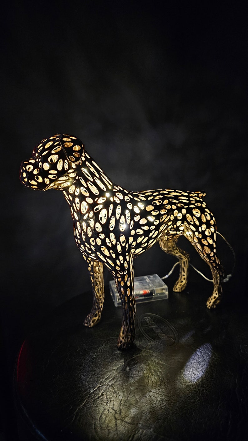 May include: A black metal dog sculpture with a light inside, creating a patterned effect. The sculpture is standing on a black surface.