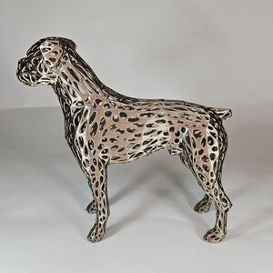 May include: A silver-colored metal sculpture of a boxer dog. The sculpture is made of a wire mesh design, creating a detailed and intricate look.