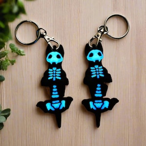May include: Two black glow-in-the-dark skeleton dachshund keychains with silver key rings.