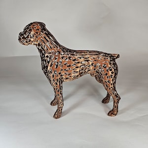 May include: A brown wireframe sculpture of a dog standing on a white surface. The sculpture is made of thin metal wires that are connected to form a three-dimensional shape.