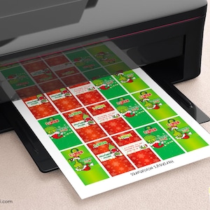 K&ouml;nnte beinhalten: Ein schwarzer Drucker druckt ein Blatt mit weihnachtlichen Etiketten. Die Etiketten zeigen eine gr&uuml;ne Figur mit Weihnachtsm&uuml;tze, roten und wei&szlig;en Text und einen rot-wei&szlig;en Schneeflockenhintergrund. Der Text "Hershey's miniatures" ist sichtbar.