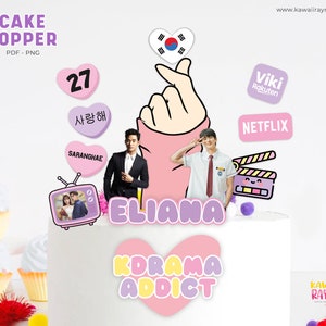 Puede incluir: Un adorno para pastel de color rosa y morado con el texto "ELIANA KOREAMA ADDICT" y un corazón con el texto coreano "SARANGHAE" que significa "Te amo". El adorno también incluye una imagen de dibujos animados de un televisor con una pareja dentro, una claqueta, una mano haciendo un corazón y una bandera de Corea del Sur.