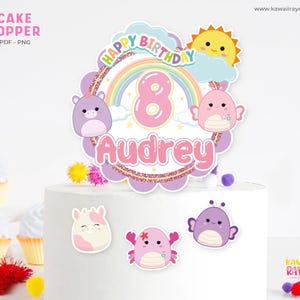 Puede incluir: Un adorno para pastel con un diseño de "Feliz Cumpleaños", un arcoíris y el número 8. El adorno está personalizado con el nombre "Audrey" en rosa. Elementos decorativos adicionales incluyen personajes de dibujos animados y un sol sonriente.