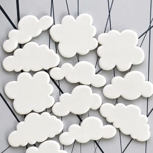 May include: A collection of twelve white, puffy cloud-shaped cutouts arranged in a scattered pattern. Each cloud features a smooth, rounded, scalloped edge design, creating a uniform appearance across the set of individual decorative pieces.