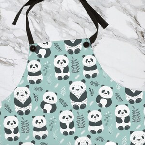 May include: A blue and white kitchen apron with a repeating pattern of pandas and leaves. The apron has adjustable black straps and two black buttons.