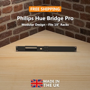 Può includere: Un Philips Hue Bridge Pro nero, progettato per rack da 19 pollici, è mostrato contro un muro di mattoni e una superficie di legno. Il testo "FREE SHIPPING" è in un riquadro arancione. Il prodotto è "MADE IN THE UK".