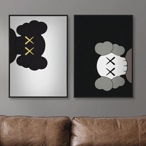 Peut inclure: Deux impressions d'art encadrées représentant des personnages de dessins animés abstraits. L'une présente une figure noire avec des os croisés jaunes sur fond blanc. L'autre présente une figure blanche avec des os croisés noirs sur fond noir.
