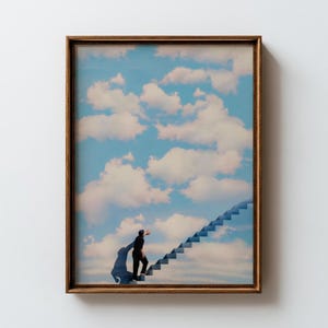 Pode incluir: Impressão artística emoldurada com uma imagem surreal de uma pessoa subindo uma escada que leva a um céu nublado. A obra de arte tem uma moldura dourada e uma paleta de cores azul e branca.