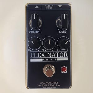 May include: A black rectangular guitar effects pedal labeled PLEXINATOR 9000 with two large knobs for volume and gain, three smaller knobs for B, M, and T, a central footswitch, a red indicator light, and text reading E.G. WONDERS BMF PEDALS.