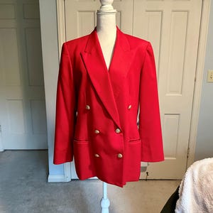 May include: A vibrant red double-breasted blazer with gold buttons. The tailored jacket features a notched lapel and two front pockets. It is displayed on a white mannequin. The blazer is a classic design.