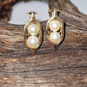 May include: A pair of gold earrings shaped like pea pods with two white pearls in each pod.