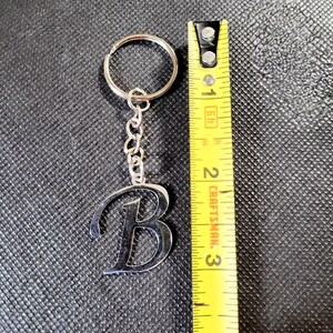 May include: Silver metal keychain with the letter "B" design. The keychain is attached to a chain and a ring. The keychain measures approximately 2.5 inches in length.