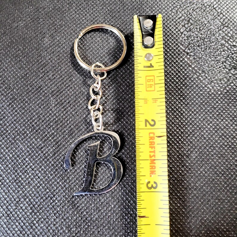May include: Silver metal keychain with the letter "B" design. The keychain is attached to a chain and a ring. The keychain measures approximately 2.5 inches in length.