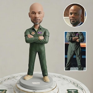 Puede incluir: Figura de un hombre con un traje de vuelo verde con los brazos cruzados. La figura tiene la cabeza calva y una pequeña barba. La base de la figura es gris con el nombre "XCHATTSONS" impreso. Hay dos imágenes más pequeñas del hombre en el fondo.