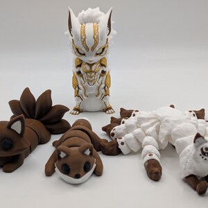 Pu&ograve; includere: Una collezione di quattro statuette di animali articolate. Una &egrave; in piedi in bianco e oro, mentre le altre tre sono in marrone o bianco, con code multiple e corpi segmentati progettati per il movimento e la posa su una superficie piana.