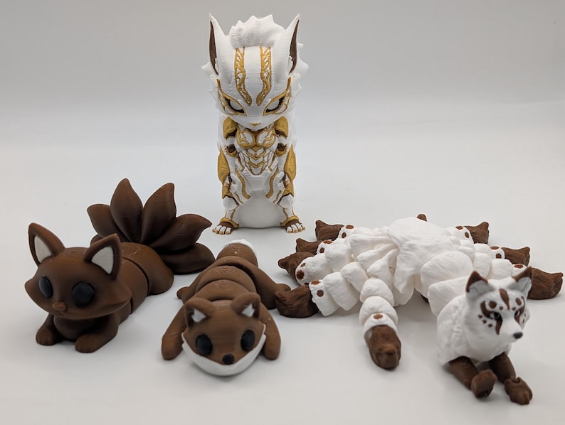 Pu&ograve; includere: Una collezione di quattro statuette di animali articolate. Una &egrave; in piedi in bianco e oro, mentre le altre tre sono in marrone o bianco, con code multiple e corpi segmentati progettati per il movimento e la posa su una superficie piana.