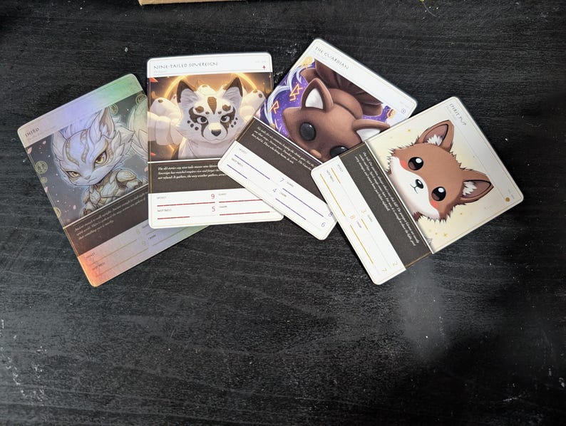 Pu&ograve; includere: Quattro carte da gioco rettangolari con creature fantastiche illustrate. Le carte mostrano personaggi chiamati Delta, Nine-Tailed Spiritfox, The Guardian e Spirit Pup, ciascuna con testo stampato, linee statistiche e illustrazioni uniche.