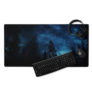 Puede incluir: Un teclado y un ratón negros con unos auriculares negros sobre una alfombrilla de ratón con una escena de bosque nocturno estrellado azul oscuro y negro.