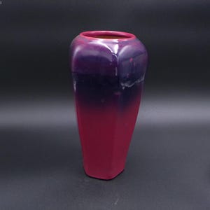 May include: A tall, hexagonal vase with a gradient color scheme. The top is a deep purple, transitioning to a vibrant magenta at the base. The vase has a smooth, glossy finish, suitable for home decor.