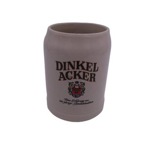 May include: A beige ceramic beer stein with a brown logo that reads "DINKEL ACKER" and the text "Brau-Erlebnis aus 200 jähriger Familientradition".