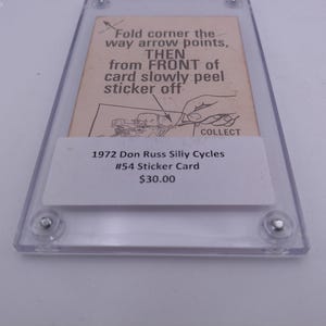 Puede incluir: Primer plano de una tarjeta de pegatina Don Russ Silly Cycles #54 de 1972 en una caja de plástico protectora. La tarjeta está valorada en 30,00 €. Las instrucciones para quitar la pegatina están impresas en la tarjeta.