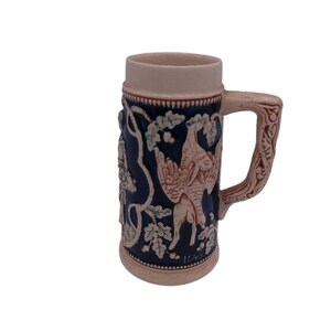 May include: A ceramic beer stein with a blue and white design featuring a bird and floral motifs. The stein has a handle and a raised design.