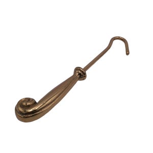 May include: A gold-toned metal hook with a decorative, curled handle. The hook is designed for hanging items.