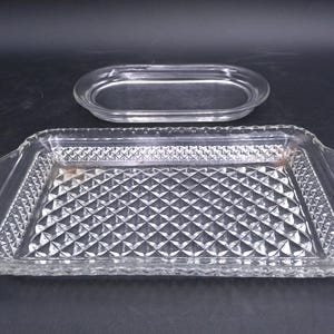 Könnte beinhalten: Zwei klare Glasservierplatten. Die größere Platte hat ein Diamantenmuster und Griffe an den Seiten. Die kleinere Platte ist oval.