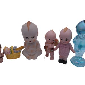 May include: A collection of five porcelain dolls.  The dolls are all dressed in different outfits.  One doll is holding a basket with a loaf of bread.  Another doll is holding a flower.  The dolls are all in various poses.