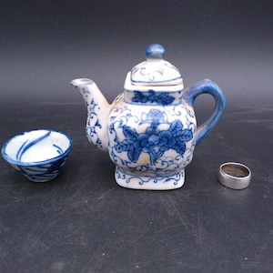 Puede incluir: Una tetera de porcelana azul y blanca en miniatura con tapa y una taza a juego. La tetera tiene un diseño floral y la taza tiene un diseño de espiral.