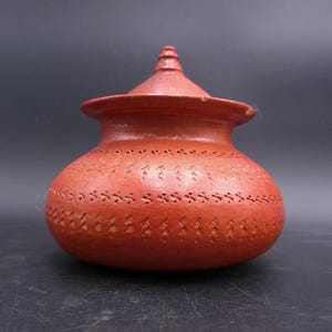 May include: A red clay pot with a lid, decorated with a repeating pattern of small lines. The pot is about 6 inches tall and 5 inches wide.