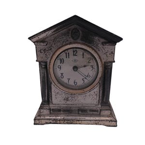 May include: An antique, off-white mantel clock with a black roof and accents. The clock face is white with black numerals and hands. The clock has a rectangular base and two columns on either side of the clock face.