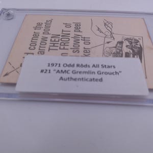 Puede incluir: Primer plano de una tarjeta de colección Odd Rods All Stars de 1971 con el AMC Gremlin Grouch. La tarjeta está autenticada y tiene instrucciones sobre cómo quitarla de su estuche protector.