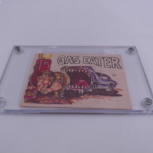 Puede incluir: Una tarjeta de intercambio vintage con una ilustración de dibujos animados de un automóvil con una boca de monstruo, etiquetada como "Gas Eater" y el número 57. Un hombre con una camisa verde está trabajando en el automóvil.