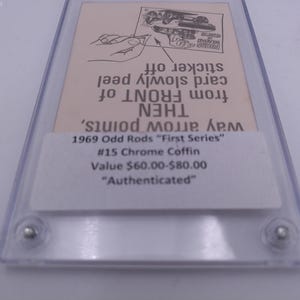 Puede incluir: Una tarjeta blanca con texto negro que describe un 1969 Odd Rods "First Series" #15 Chrome Coffin. La tarjeta tiene instrucciones sobre cómo quitar una pegatina de la parte delantera de la tarjeta. El valor de la tarjeta se indica como 48,00 € a 64,00 €. La tarjeta está etiquetada como "Autenticada".