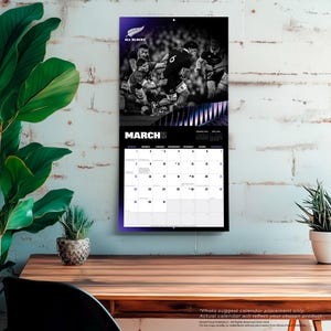 May include: A black and white All Blacks rugby calendar for March. The calendar features a photo of rugby players in action at the top, with the month of March prominently displayed. The calendar is hanging on a white wall.