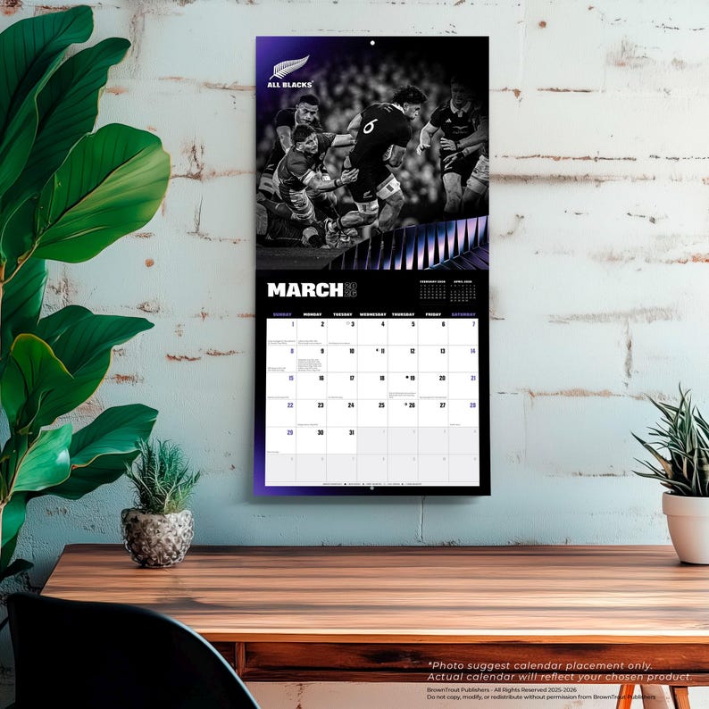 May include: A black and white All Blacks rugby calendar for March. The calendar features a photo of rugby players in action at the top, with the month of March prominently displayed. The calendar is hanging on a white wall.