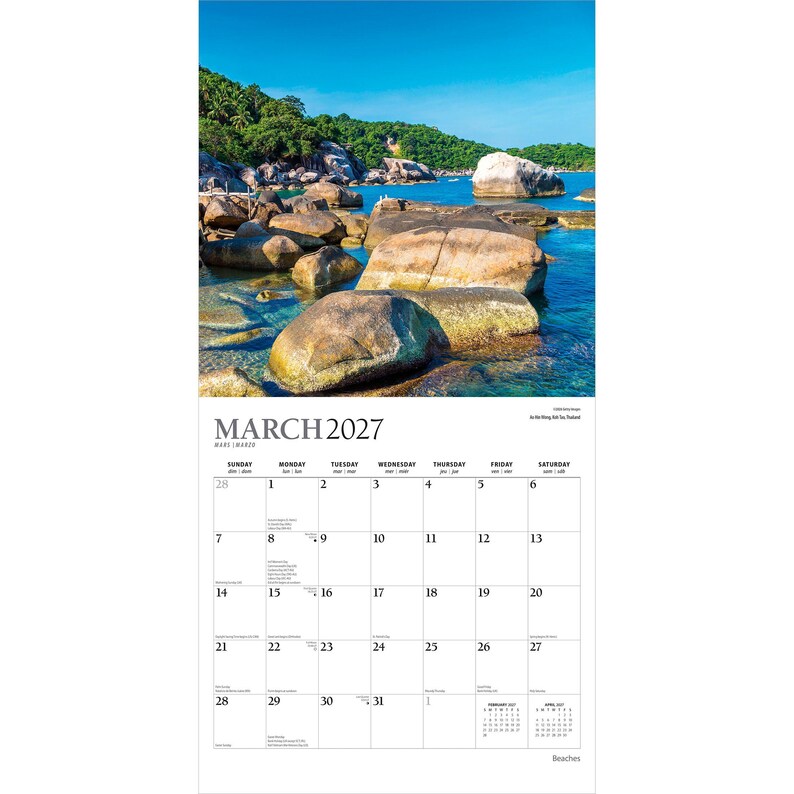 May include: A wall calendar for March 2027 featuring a photograph of a tropical coastline with large tan boulders in clear blue water under a bright sky. The calendar grid displays the month, days of the week, and dates in black text on white.