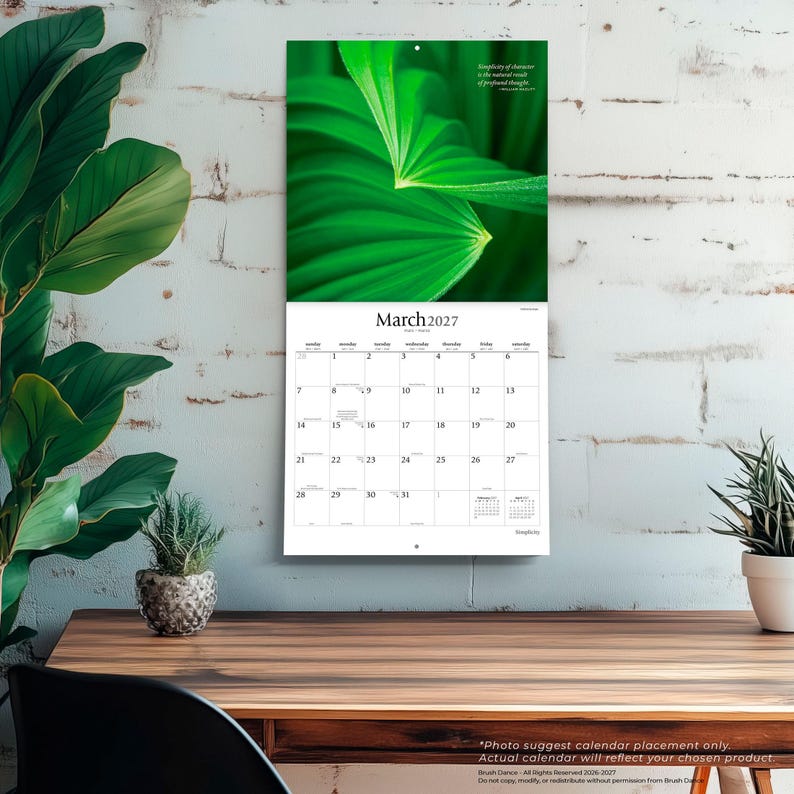 May include: A wall calendar for March 2027 featuring a vibrant green leaf photograph at the top. The calendar grid displays the days of the month with the text March 2027 at the top and a small quote in the upper right corner of the image section.