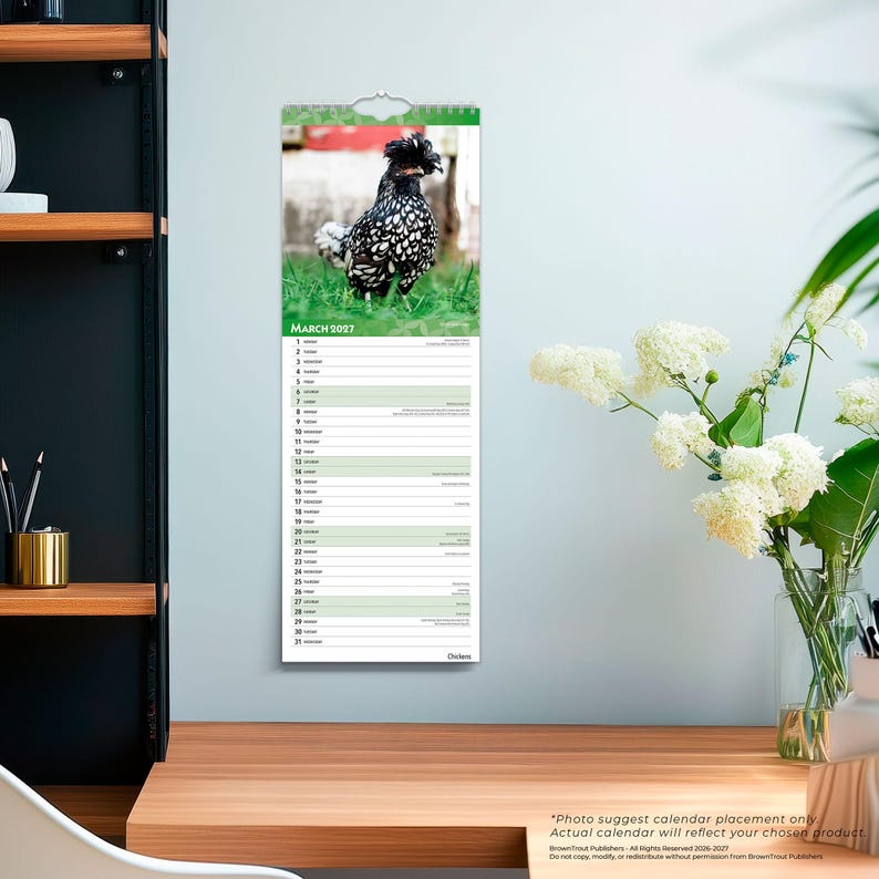 Op de afbeelding: Een verticale wandkalender voor maart 2027 met een foto van een zwart-wit gespikkelde kip met een kuif van veren op de kop, staand in groen gras. Het kalenderraster vermeldt de data 1 tot en met 31 met horizontale lijnen.