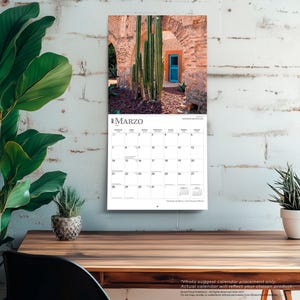 May include: A wall calendar for March 2027 featuring a photograph of tall green cacti in front of a rustic brick archway with a bright blue door. The calendar grid displays the month of March with days numbered one through thirty-one.