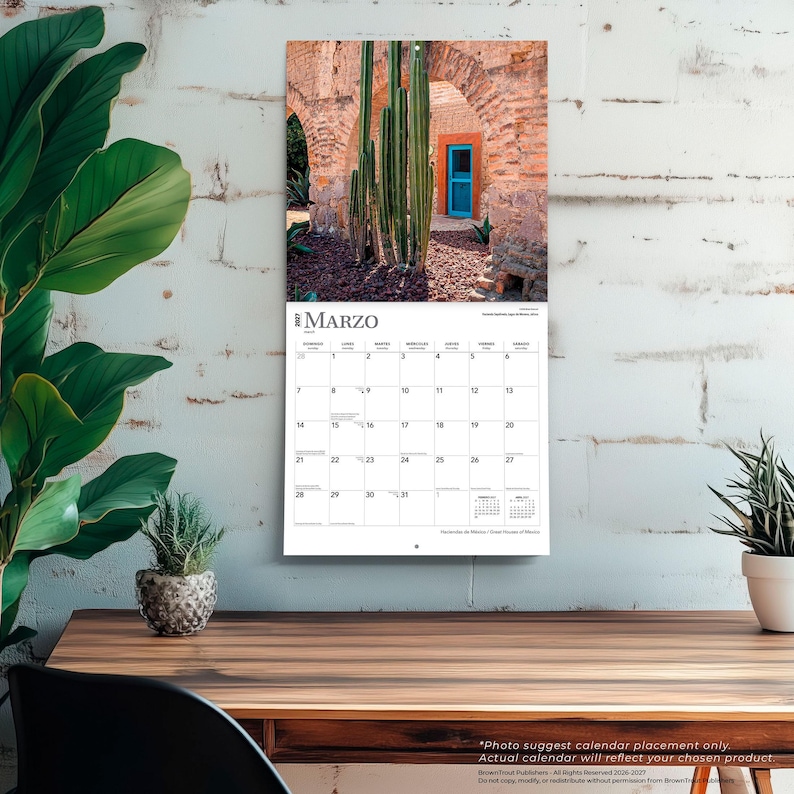 May include: A wall calendar for March 2027 featuring a photograph of tall green cacti in front of a rustic brick archway with a bright blue door. The calendar grid displays the month of March with days numbered one through thirty-one.